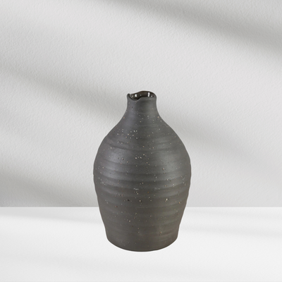 A black Eos Blooms Tikal Vase with a small spout sits on a white surface against a light background.