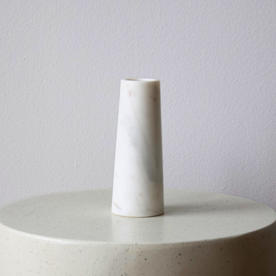 The Tuscany Marble Vase by Eos Blooms sits on a round, speckled surface against a plain wall.