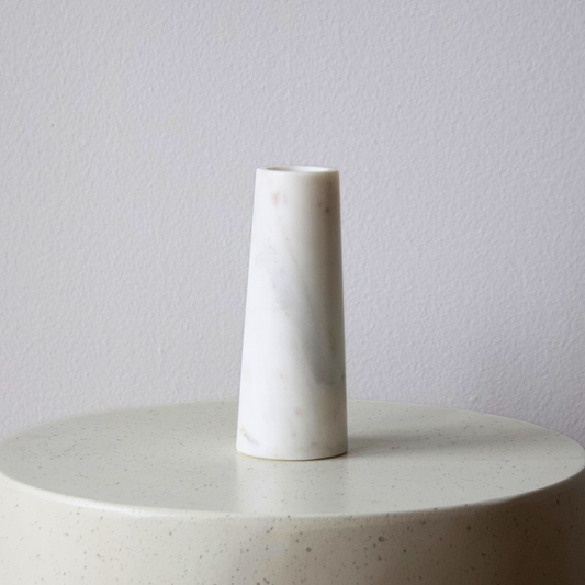 The Tuscany Marble Vase by Eos Blooms sits on a round, speckled surface against a plain wall.