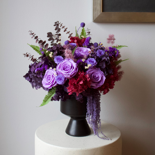 Ultraviolet Petite Forever Roses by Eos Blooms in a black vase on a white table.