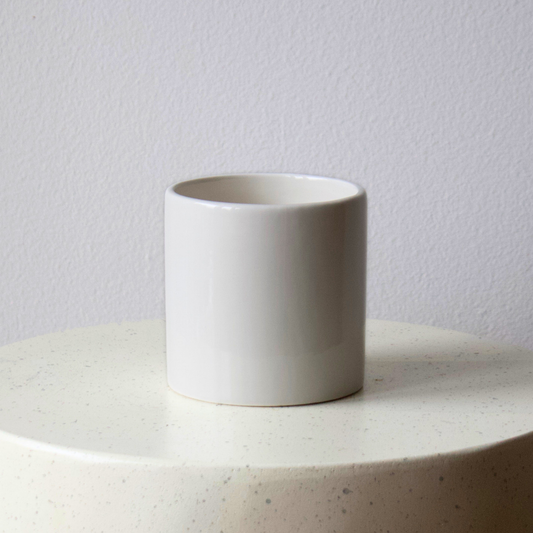 Eos Blooms’ White Cylinder and a white cup rest on a round, light-colored surface.