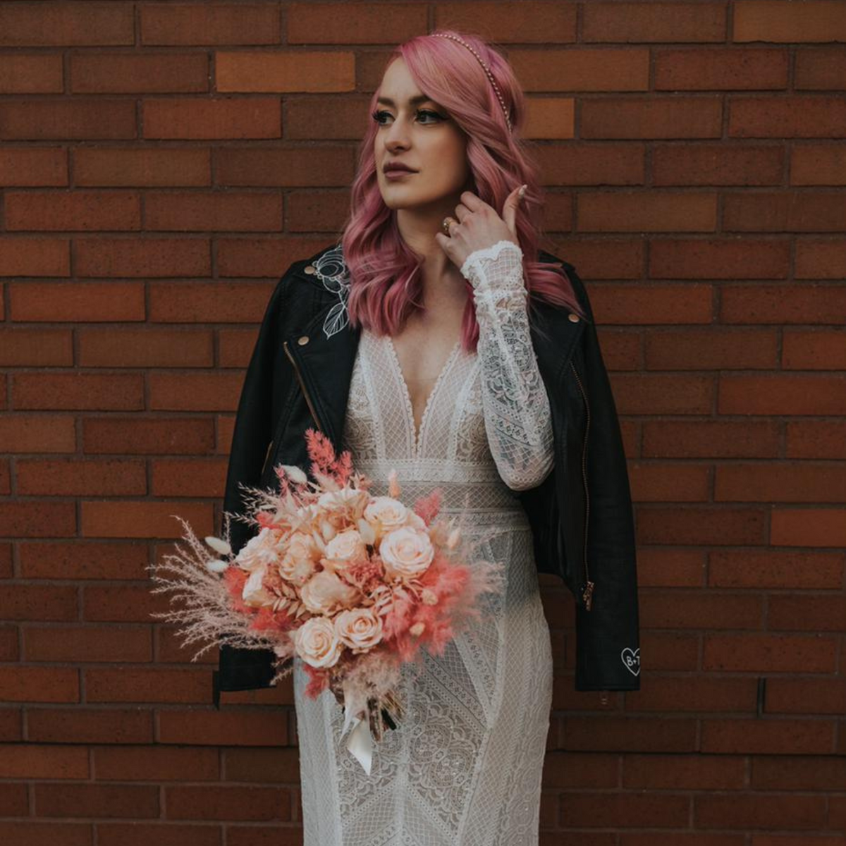 Bride with pink hair holds "The Promise" bouquet by Eos Blooms, in lace dress and black jacket.