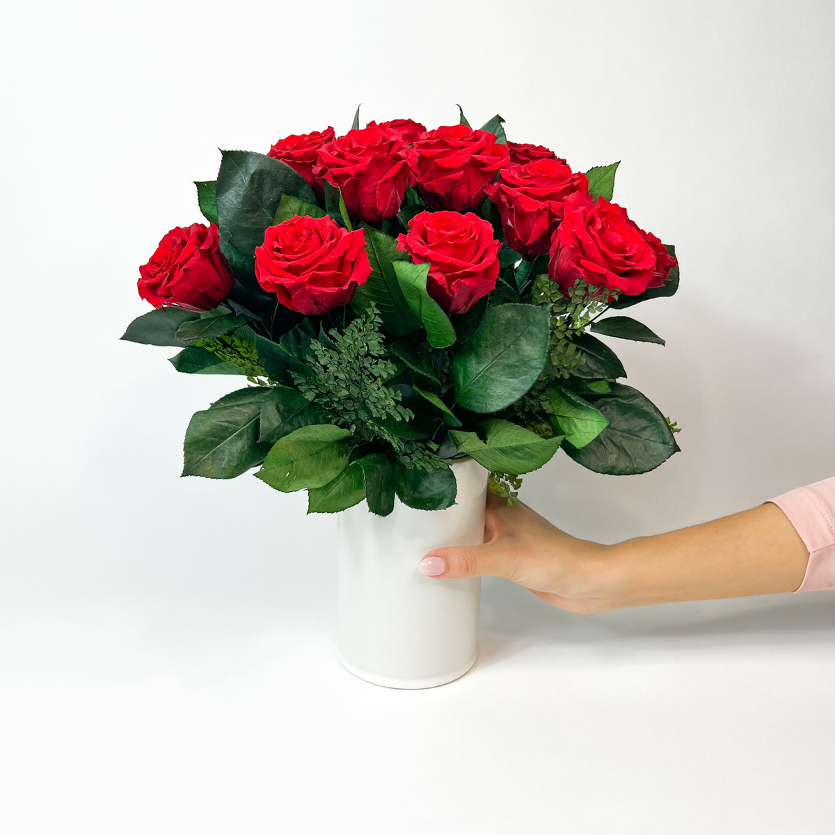 A hand holds Eos Blooms’ Love Story white vase with red roses and green leaves.