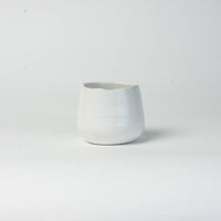 A small, white Eos Blooms ceramic vase on a plain white background.
